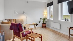 A modern living room with a sofa, a wooden chair, a small table, a floor lamp, a potted plant, and a TV on a stand. - "Truels" - 2km from the sea by Interhome (Tranekær)