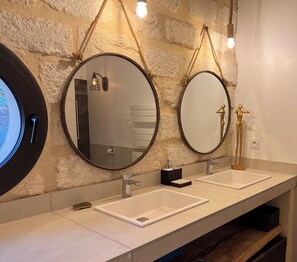 Un baño con dos lavamanos, dos espejos redondos y una lámpara.