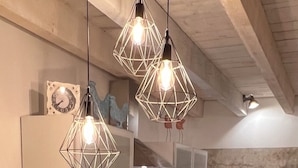 A modern kitchen with a central island, hanging geometric light fixtures, and a coffee machine.