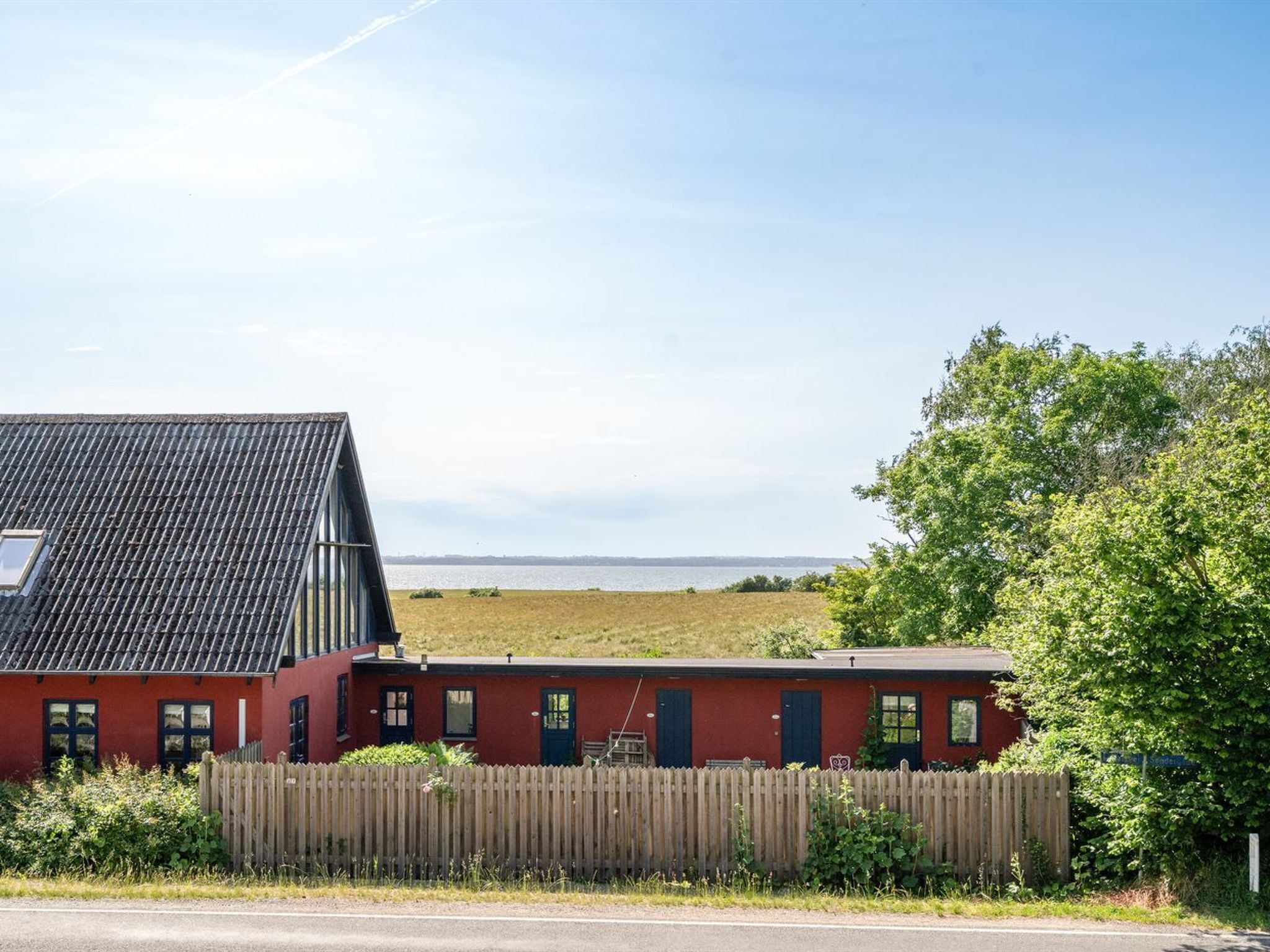 Un bâtiment rouge avec un toit en pente, une clôture en bois et une vue sur une étendue d’eau.