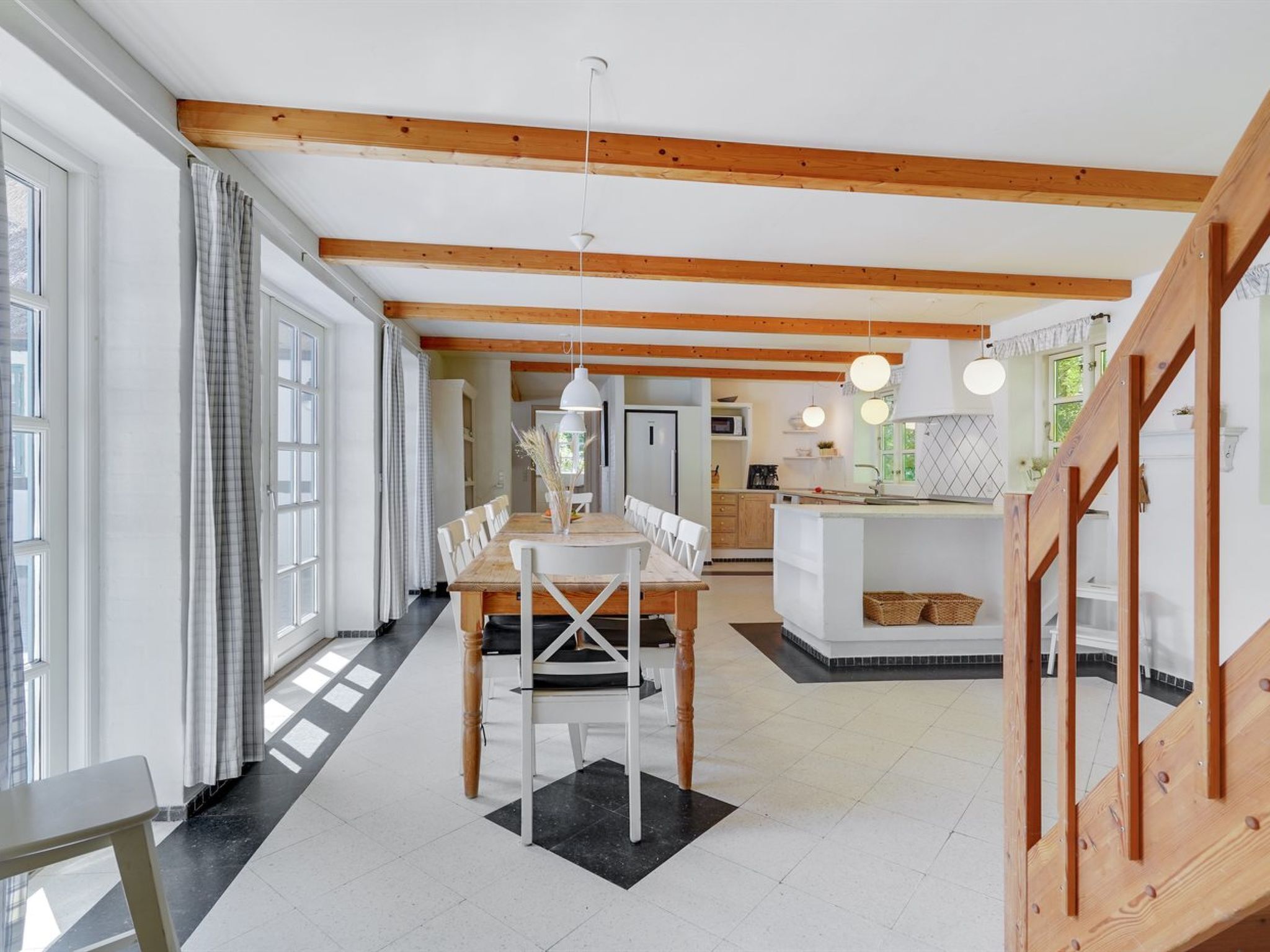 Une cuisine spacieuse avec des poutres en bois, un coin repas avec une table et des chaises, et une vue sur le salon attenant.