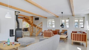 A spacious living area with a wooden staircase, a fireplace, and a kitchen in the background. - "Sirkku" - 320m from the sea by Interhome (Tranekær)