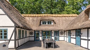 A traditional building with a thatched roof, white walls with black timber framing, and a central courtyard with a table and chairs. - "Sirkku" - 320m from the sea by Interhome (Tranekær)