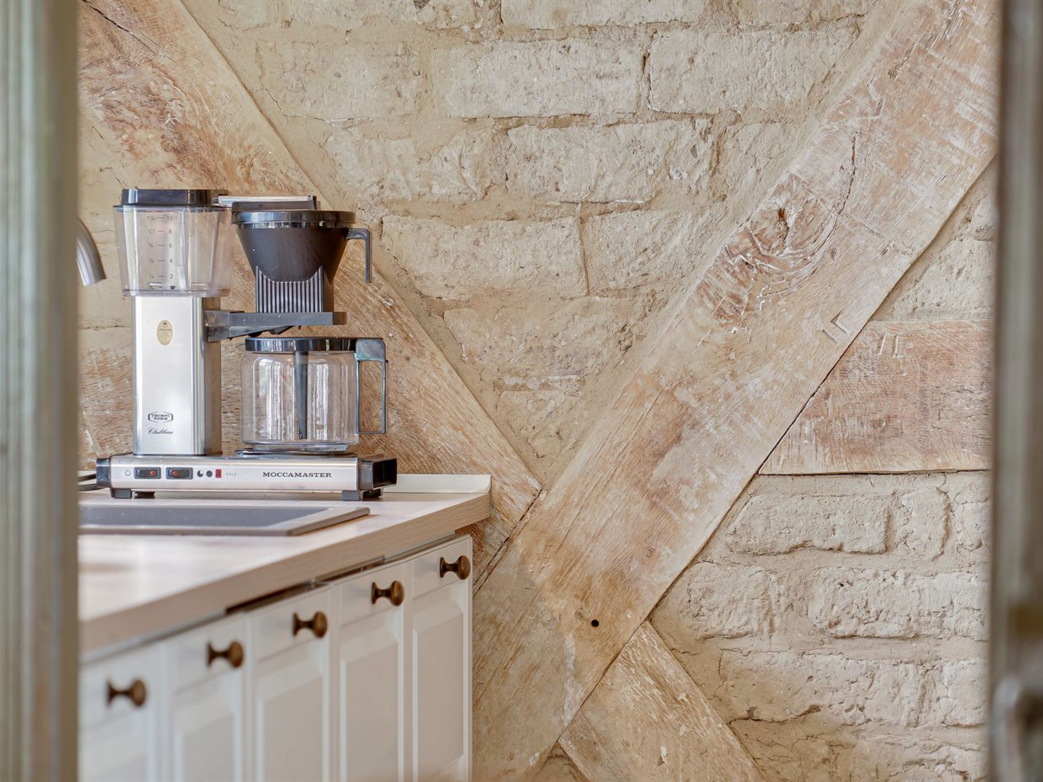 A kitchenette with a coffee maker, a scale, and a glass container on a countertop.