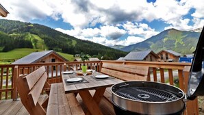 Een houten terras met een barbecue en eettafel, ingericht voor buiten eten, met uitzicht op een bergachtig landschap.