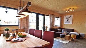 Een moderne woonkamer met een houten eettafel, rode stoelen, een bank en een groot raam.