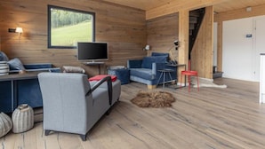 En mysig stuga med träpanel på väggarna, en soffa, en tv och utsikt över naturen.
