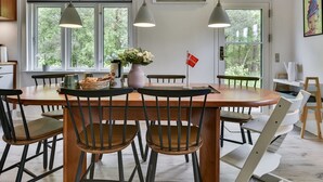 A dining area with a wooden table and chairs, large windows, and an air conditioning unit on the wall.