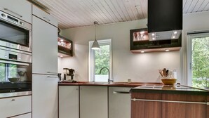 A modern kitchen with white cabinetry, a Bosch oven, a coffee machine, and a large window offering a view of greenery.