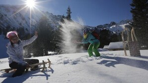 A snowy outdoor scene with a wooden sled and a person sitting on it.