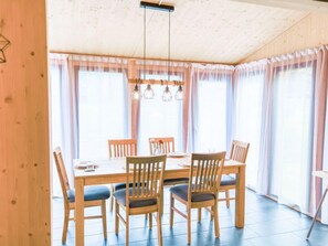 A dining area with a wooden table and chairs, large windows with sheer curtains, and hanging pendant lights.