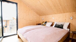 A bedroom with a large bed, wooden walls, and a view through a glass door.