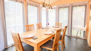A dining area with a wooden table and chairs, large windows with sheer curtains, and a hanging light fixture.