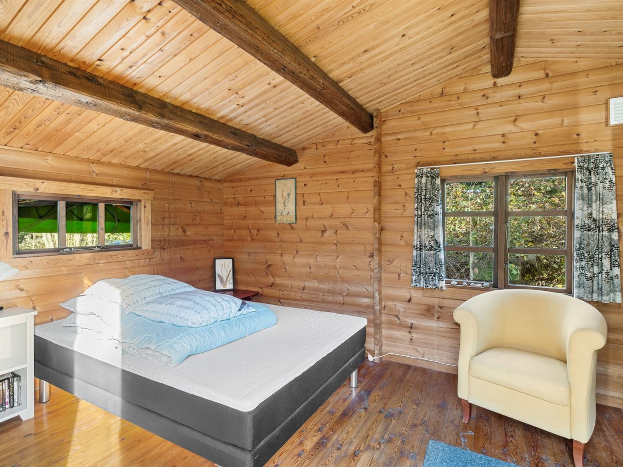 Un dormitorio de cabaña de madera con una cama, una silla, un ventanal y una estantería.