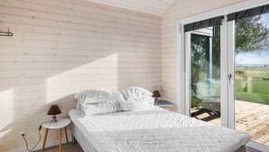 Ett sovrum med en säng, ett litet bord med en lampa och utsikt över utomhusmiljön genom en skjutdörr.