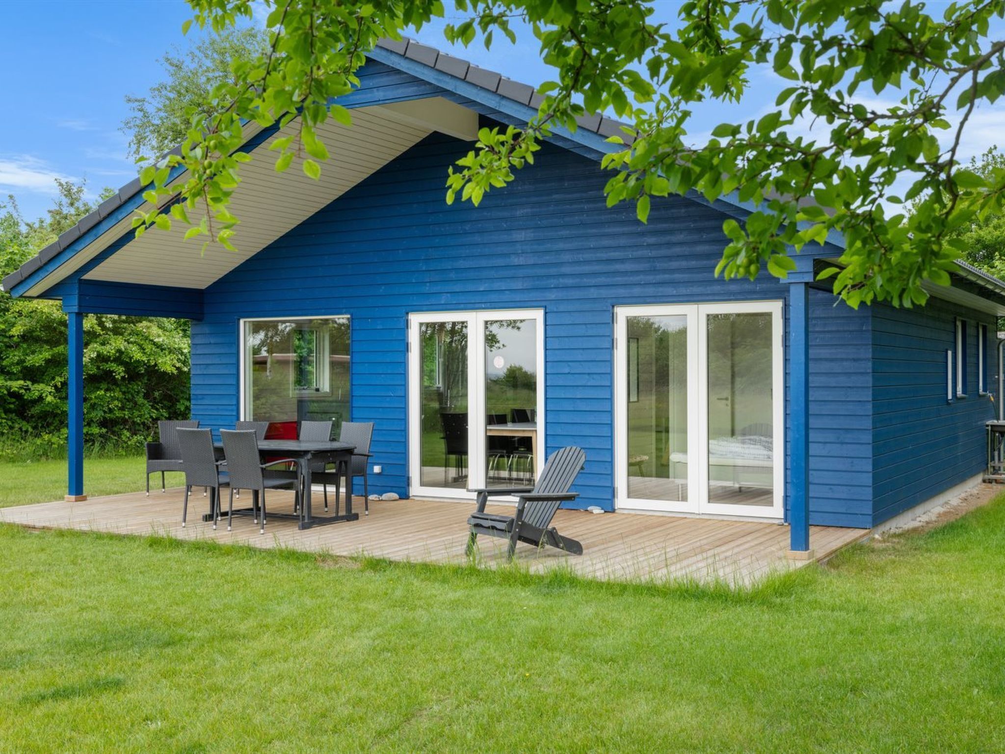 Ein blaues Haus mit überdachter Terrasse, einem Esstisch mit Stühlen und einem Rasen.