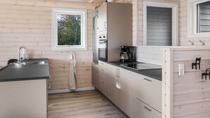Ett kompakt kök med träpanel på väggarna, ett fönster med utsikt över träd och moderna vitvaror.