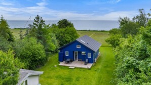 Ett blått hus med en veranda, omgivet av frodig grönska och med utsikt över havet.