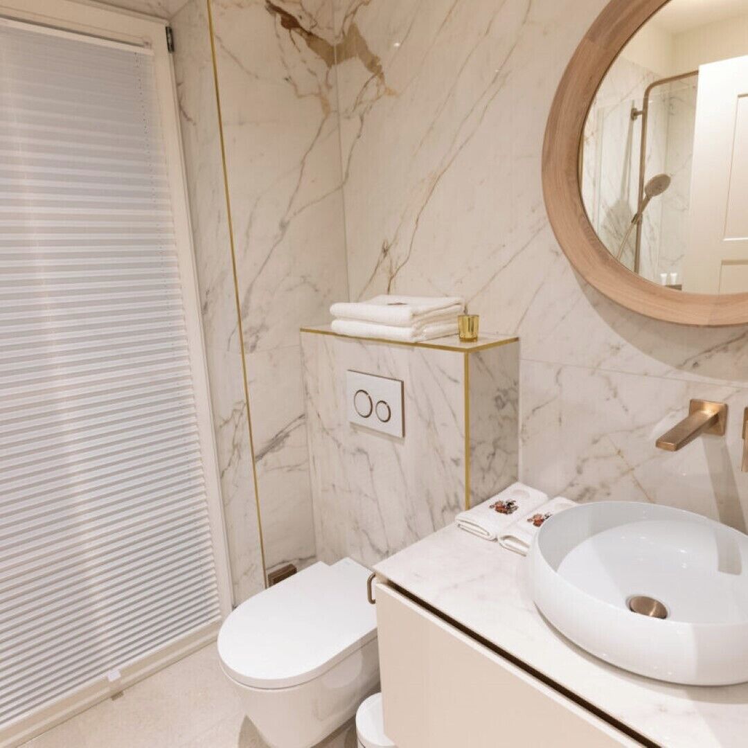A modern bathroom with a marble floor, a white sink with a gold faucet, and a toilet.