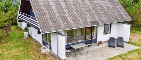 Een modern huis met een schuin dak, een overdekte patio met twee stoelen en een kleine tuin.