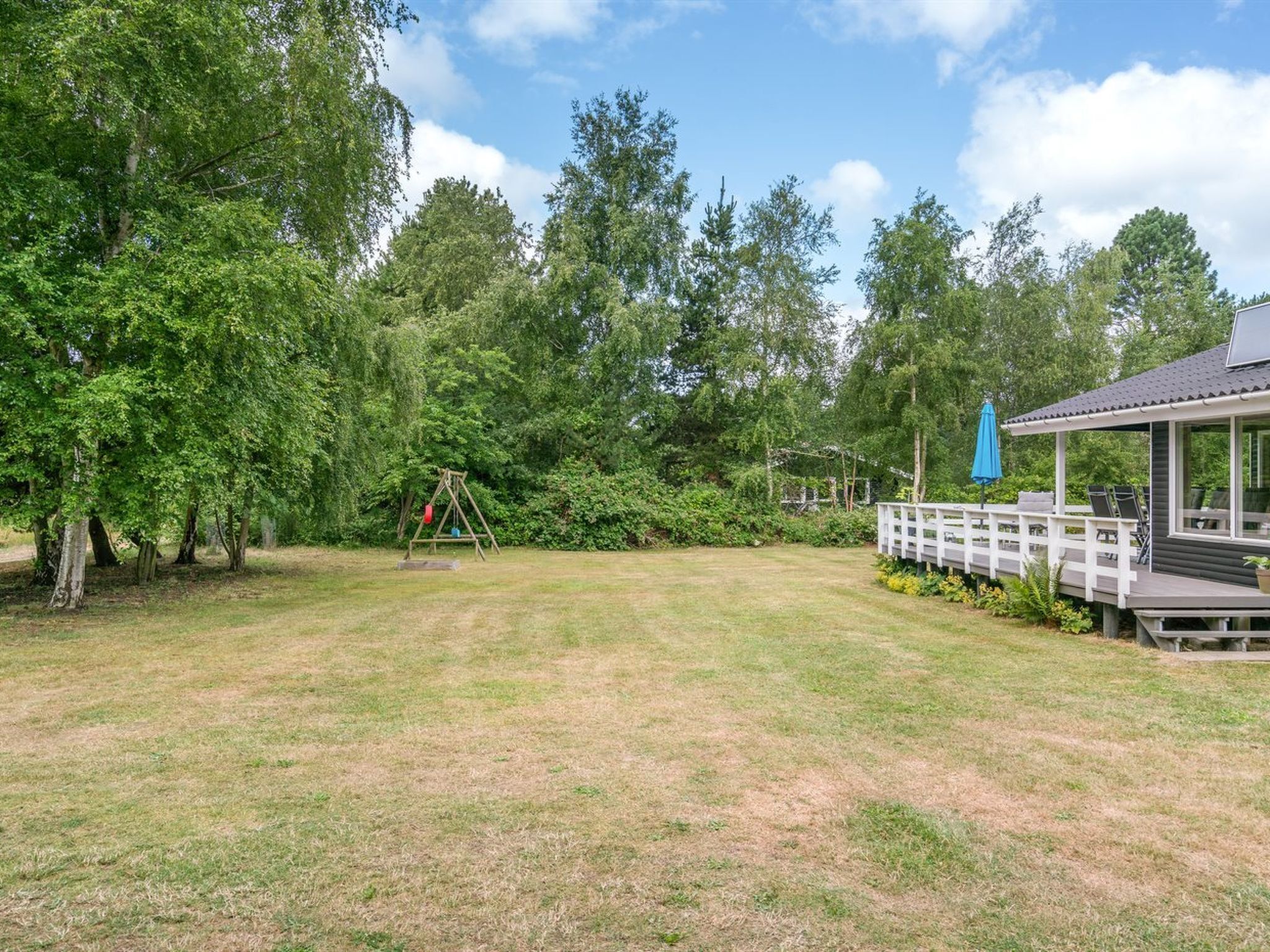 A backyard with a swing set, a covered deck, and a gazebo.