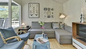 Un salon chaleureux avec un canapé, des fauteuils, un téléviseur et des œuvres d’art accrochées au mur.