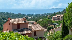 Zona residencial costera con casas de techo de teja y abundante vegetación, con vista al mar.