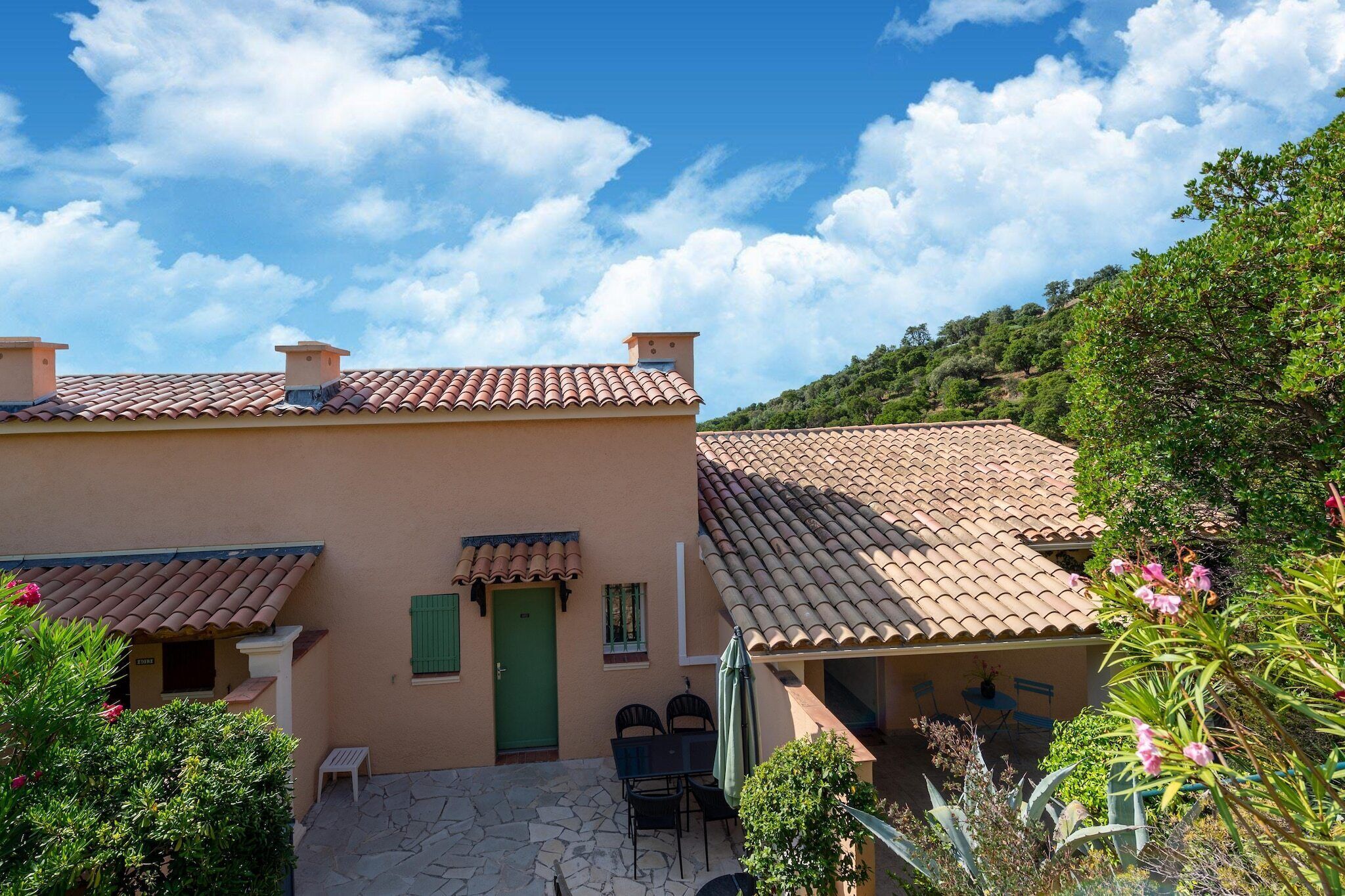 A building with a tiled roof, a green door, and a patio area with chairs and a table.