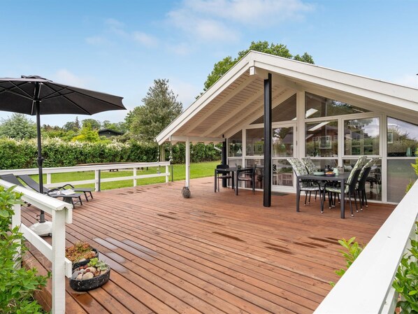 Una terraza cubierta al aire libre con zona de comedor, barandillas blancas y estructura de pérgola.