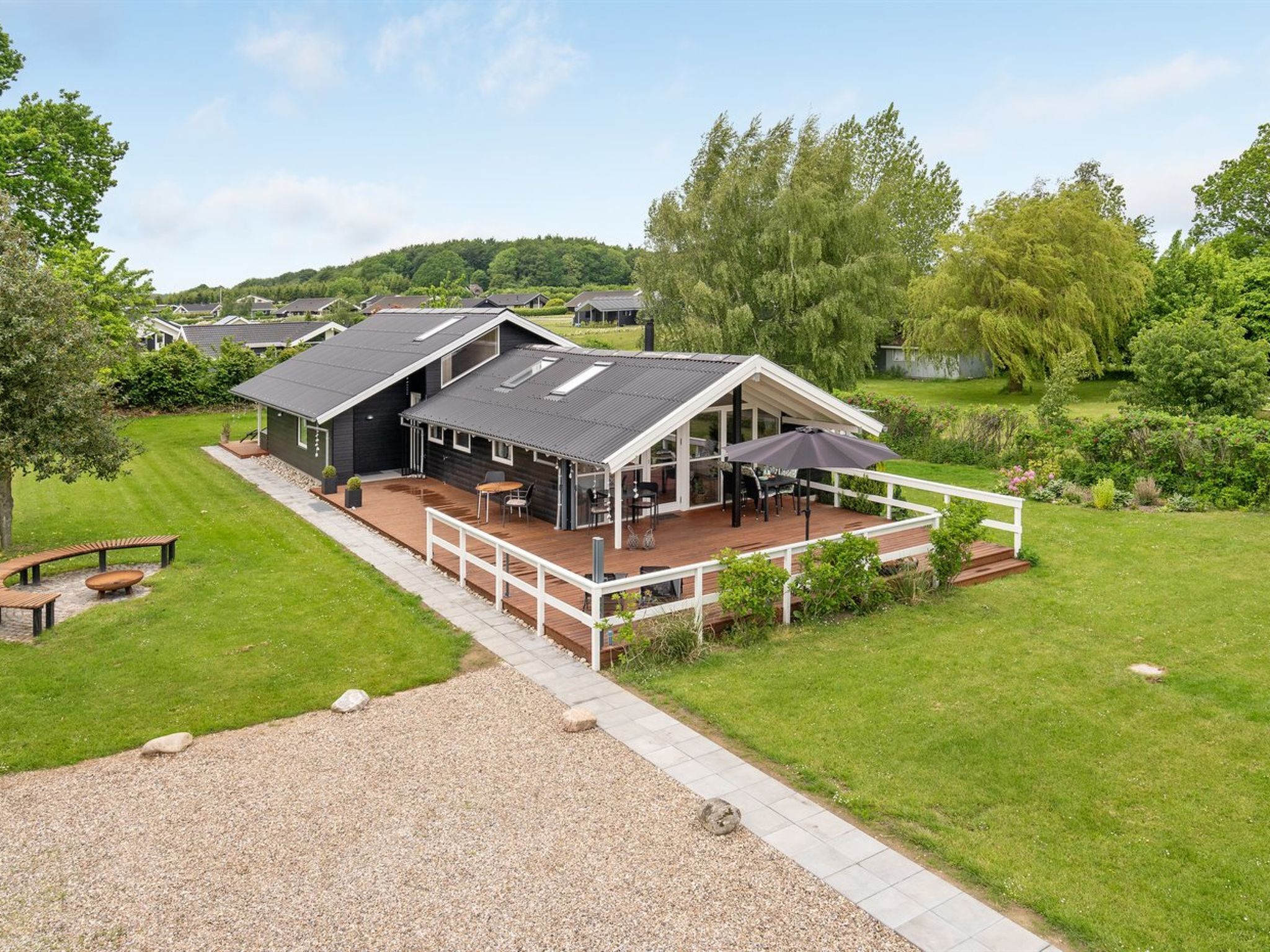 Une maison moderne dotée d’une terrasse, entourée d’une végétation luxuriante et située dans un paysage vallonné.
