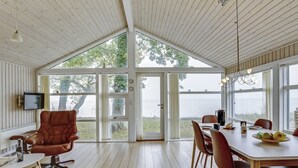 A spacious room with a large dining table, leather chairs, and a view of a body of water through large windows.
