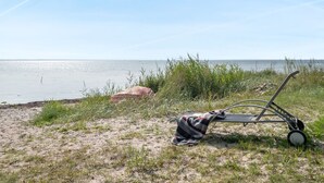 A beach with a beach chair and a blanket, a sandy shore, and a calm sea under a clear sky.