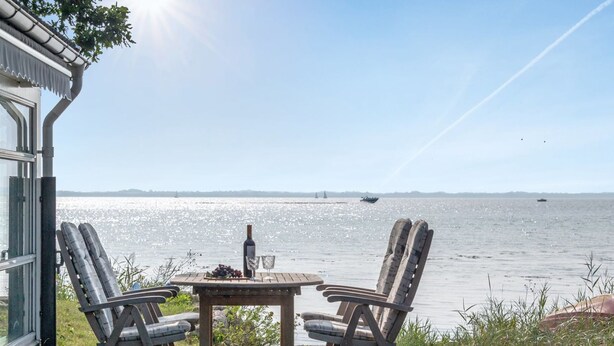 A wooden deck with two chairs and a table, overlooking a calm body of water with boats and distant land.