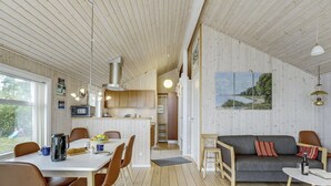 A spacious living area with a dining table, chairs, a sofa, and a coffee table. There is a kitchen area with cabinets and a stove. The room has wooden floors and a large window.