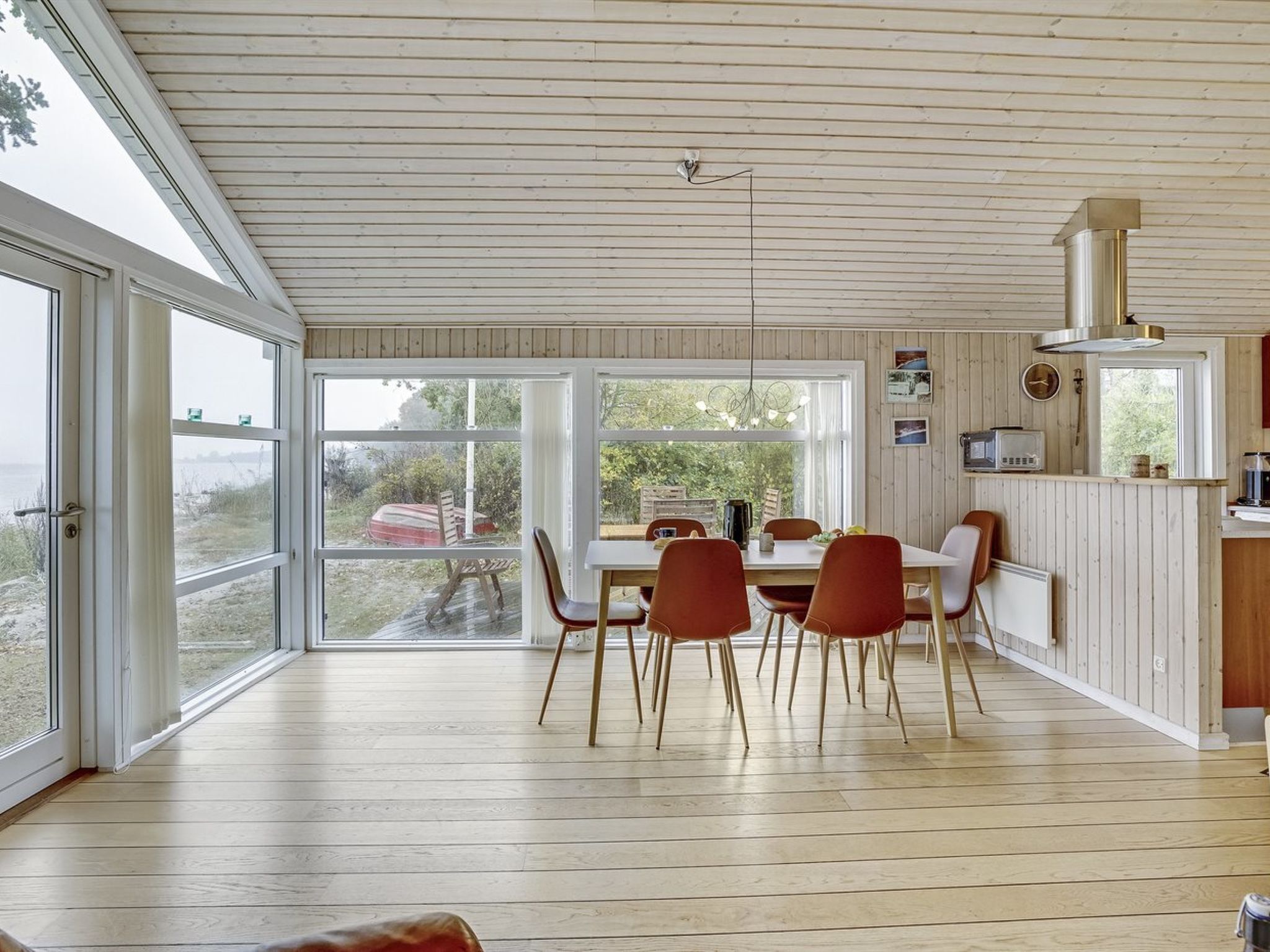 Un grand espace à manger avec une table et des chaises en bois, de grandes fenêtres donnant sur l’extérieur, et un coin cuisine équipé d’une cuisinière et d’un four à micro-ondes.