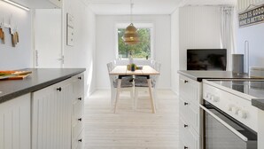 Una cocina moderna con armarios blancos, un comedor con mesa de madera, y un amplio ventanal que proporciona luz natural.