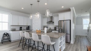 A modern kitchen with white cabinets, stainless steel appliances, and a central island with bar stools. - Luxury Hilton Head Marsh View Home | Pool & Kids' Loft (Hilton Head Island)