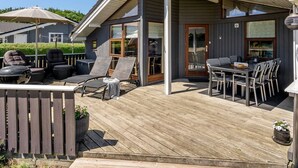 Una terraza al aire libre techada con sillones, una mesa y plantas en macetas.