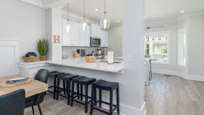 A modern kitchen with white cabinets, a central island with stools, pendant lighting, and a view to the outside. - 69 Heated Pool | Kids Retreat | Near Beach | Sleeps Big (Hilton Head Island)