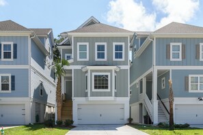A row of two-story townhouses with a central bay window, a front garage, and a small front yard with a palm tree.