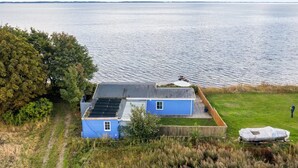 Une maison bleue dotée de panneaux solaires, un jardin clos et une vue sur l’eau.