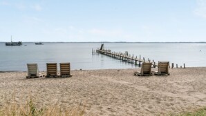 Una playa con sillas de madera y un muelle de madera que se adentra en el agua.