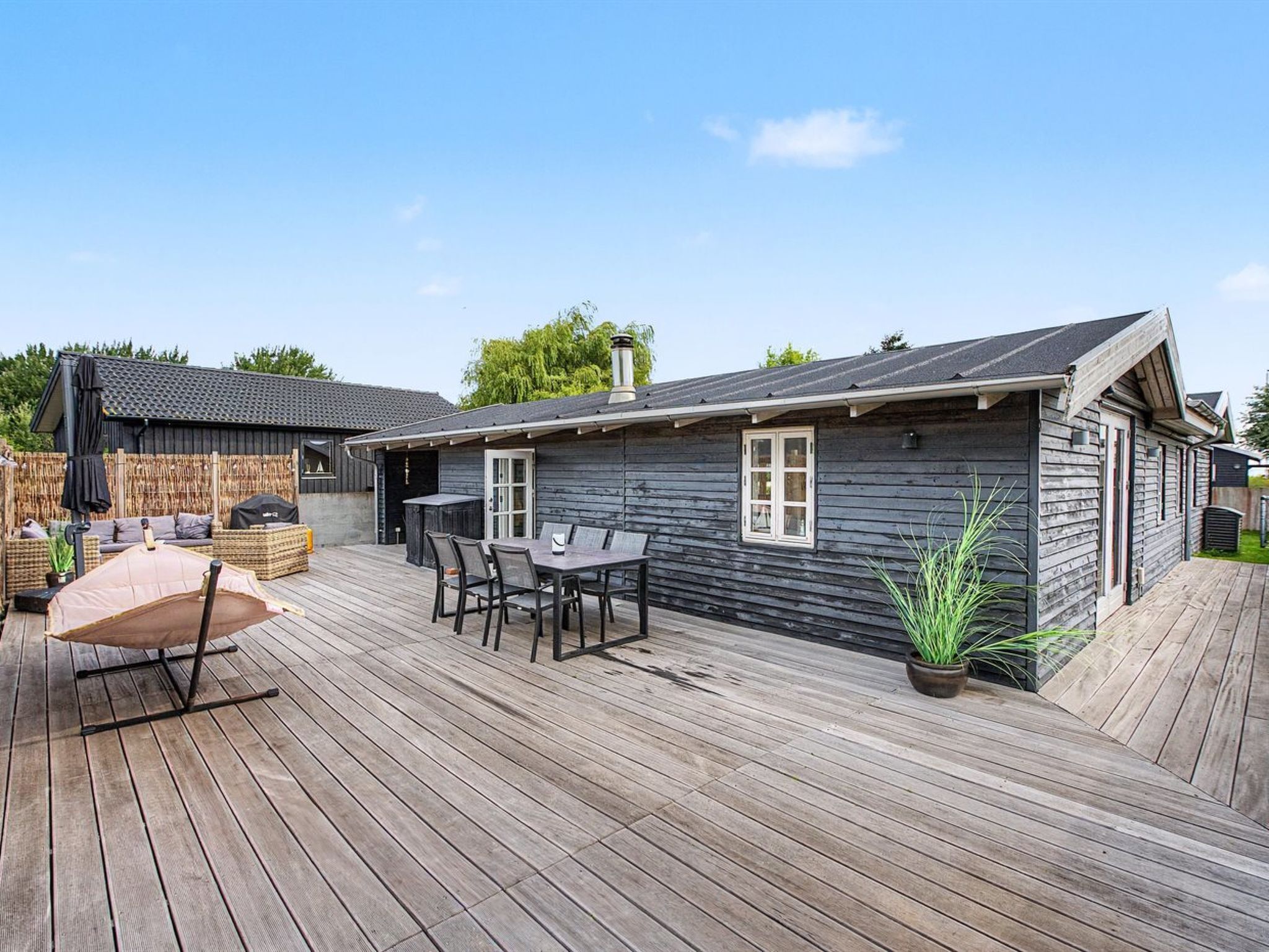 Een houten terras met een tafel, stoelen, een overdekte zithoek en een bloempot.