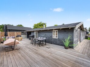 A wooden deck with a table and chairs, a covered seating area, and a potted plant.