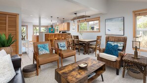 A spacious living area with a dining table, multiple chairs, a coffee table, and a wicker armchair. - Beachcomber Cottage - Short Distance to Beach 2 Bedroom - 2 Bath (Pacific City)