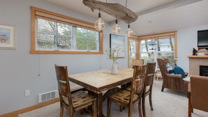 A dining area with a wooden table and chairs, pendant lights, and a fireplace. - Beachcomber Cottage - Short Distance to Beach 2 Bedroom - 2 Bath (Pacific City)