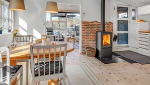 Una cucina moderna con una stufa a legna centrale, un'area pranzo con tavolo e sedie in legno, e un ambiente luminoso e soleggiato con ampie finestre.