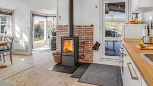 Una cucina moderna con stufa a legna, zona pranzo con tavolo e sedie, e vista all'esterno attraverso ampie finestre.
