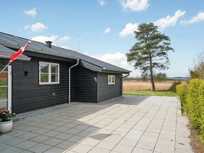 A black house with a tiled patio, a red flag, and a tree in the background. - "Antti" - 350m from the sea by Interhome (Millinge)