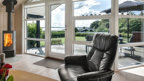 A spacious room with a large glass door leading to an outdoor area, a black leather chair, and a wood-burning stove. - "Rathi" - 250m from the sea by Interhome (Haarby)